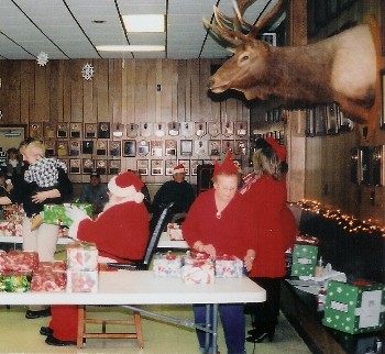 Santa (Ned Goff) gets ready to hand out another gift at the 2007 Children's Christmas party while his helper, Muriel Carpenter, gives him a hand under the "watchful eye" of the mounted elk.